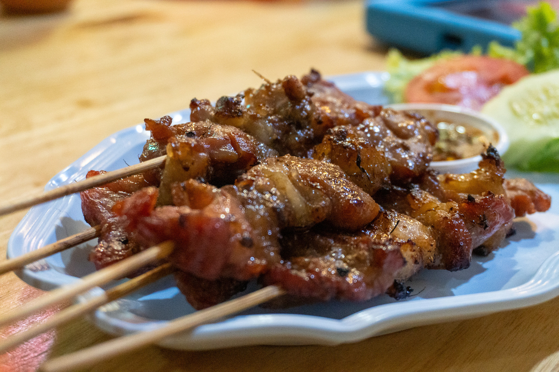 Auto-generated description: Grilled skewers of marinated meat are served on a plate with a side of dipping sauce and fresh vegetables.