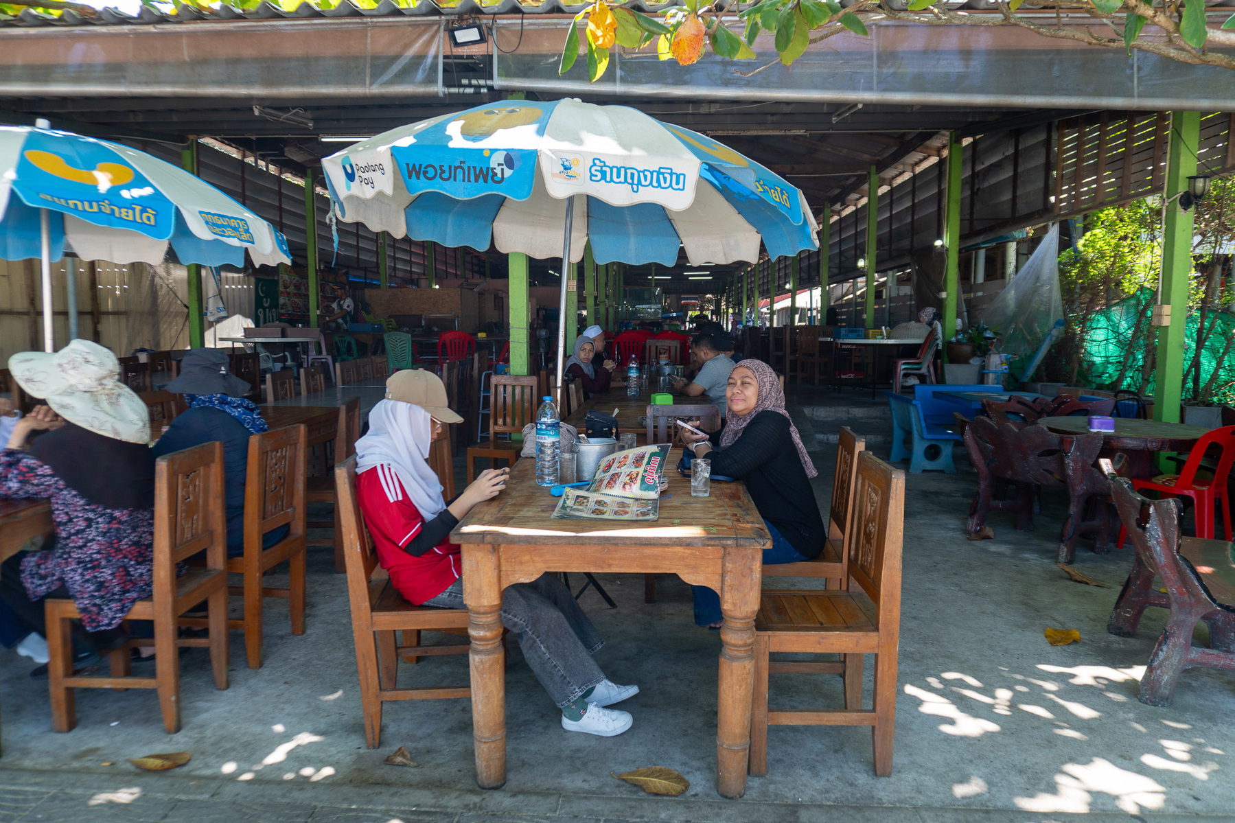 Auto-generated description: People are sitting at a wooden table under umbrellas in an outdoor café or restaurant setting.