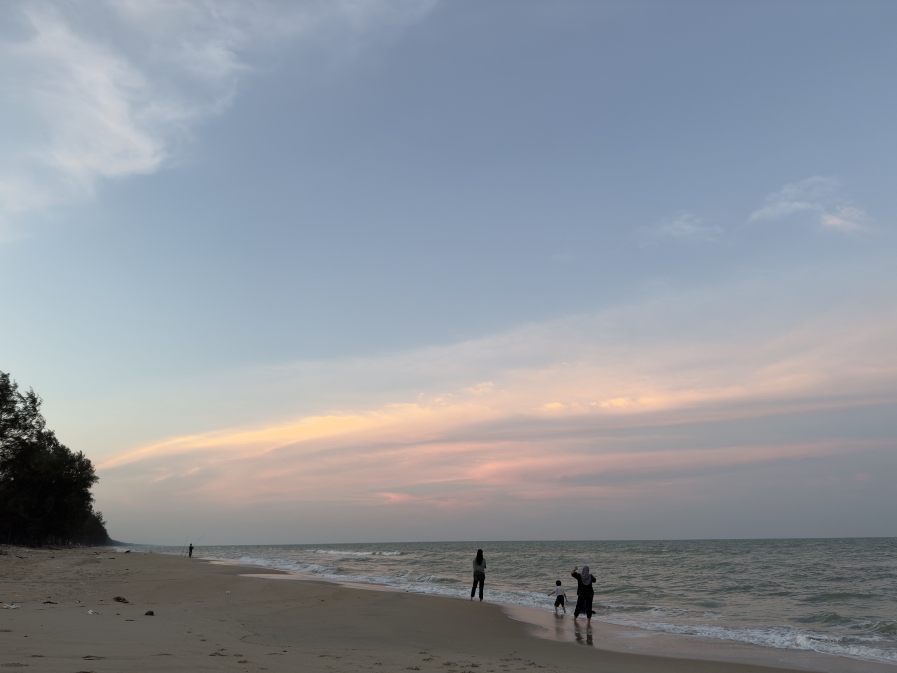 Auto-generated description: A serene beach scene at sunset features a few people strolling along the shoreline under a pastel sky.